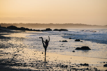 Silhouetted female ballet dancer poised on one leg at sunset on beach, Los Angeles, California, USA - ISF06707