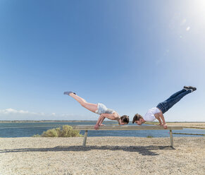 Couple practising partner yoga on beach bench - ISF06712