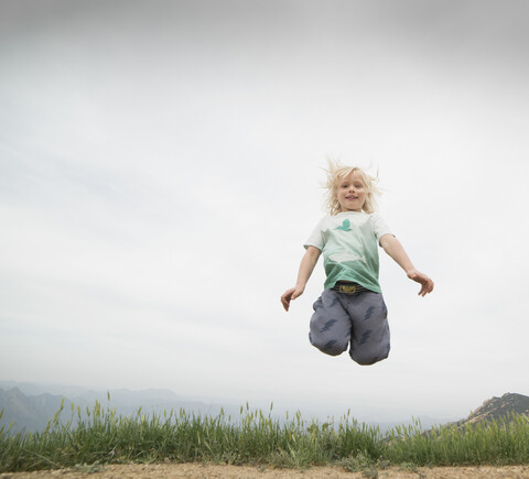 Junge springt in der Luft und schaut lächelnd in die Kamera, lizenzfreies Stockfoto