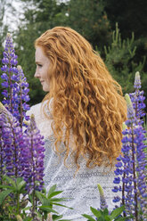 Rückansicht einer jungen Frau mit langen roten Haaren inmitten lila Wildblumen - ISF06735