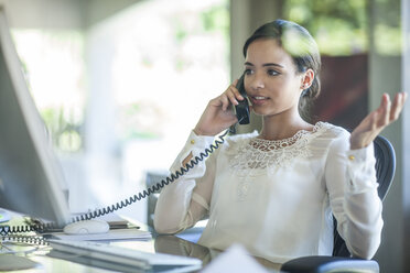 Businesswoman talking on landline telephone at office desk - ISF06741