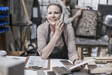Handwerkerin spricht in der Werkstatt für Antiquitätenrestaurierung mit ihrem Smartphone - ISF06775