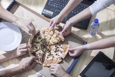 Overhead view of office workers hands selecting pizza slice from desk - ISF06784