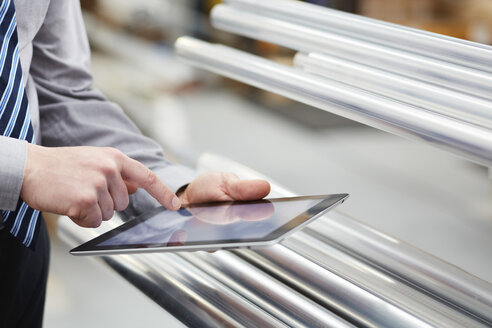 Nahaufnahme eines Arbeiters, der Metallstangen mit Hilfe eines digitalen Tablet-Touchscreens in einer Rollladenfabrik einlagert - CUF18040