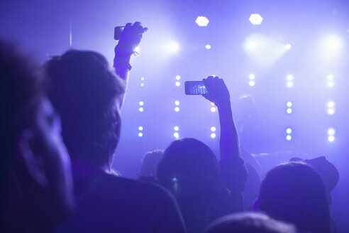 Rückansicht einer Gruppe im Club, die mit erhobenen Armen ein Konzert mit dem Smartphone filmt - CUF18056