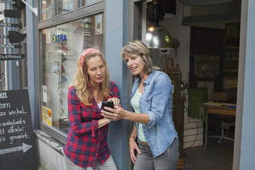 Women standing in shop doorway looking at smartphone - CUF18058