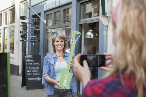 Ein Freund fotografiert eine Frau vor einem Geschäft mit einem offenen Schild, lizenzfreies Stockfoto
