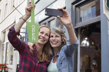 Frauen vor einem Geschäft mit offenem Schild machen ein Selfie mit ihrem Smartphone - CUF18063