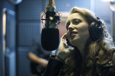 Female musician in recording studio, singing into microphone - ISF06822