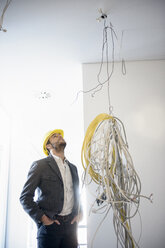 Businessman looking up at cables hanging from new office ceiling - CUF18118