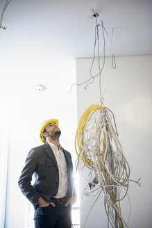 Geschäftsmann schaut auf die Kabel, die von der Decke des neuen Büros hängen - CUF18118