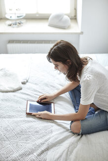 Junge Frau sitzt auf dem Bett und liest auf einem digitalen Tablet - CUF18219