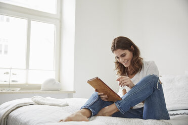 Beautiful young woman sitting on bed using digital tablet - CUF18232