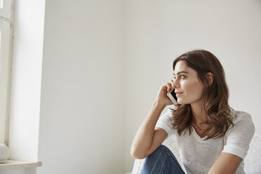 Young woman sitting on bed using smartphone - CUF18234