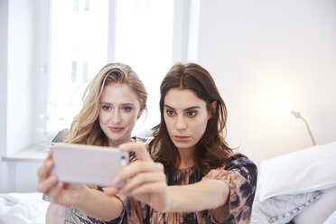 Zwei junge Frauen sitzen auf dem Bett und machen ein Smartphone-Selfie - CUF18253