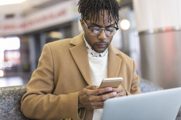 Junger Geschäftsmann sitzt im Bahnhof und schreibt eine SMS auf seinem Smartphone - ISF06904