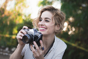 Mid adult woman taking photographs, outdoors, smiling - ISF06929