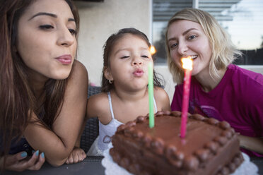 Young girl sitting with family, blowing out candles on birthday cake - ISF06944