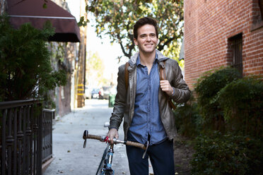 Happy young man strolling with cycle on sidewalk - ISF06964