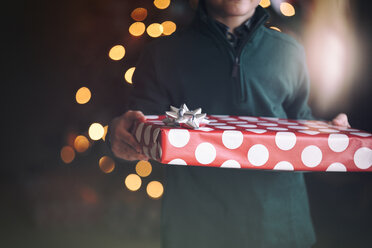 Abgeschnittene Ansicht eines Jungen vor einem Weihnachtsbaum mit einem Geschenk - ISF06966