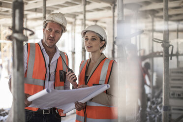 Female and male builders with blueprint on construction site - ISF06979