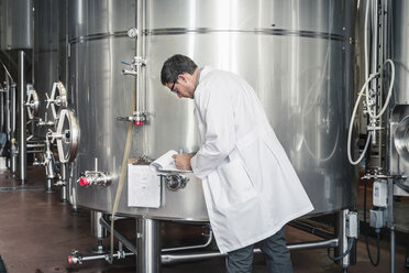 Seitenansicht eines Brauers in einer Brauerei, der einen Laborkittel trägt und auf einem Klemmbrett schreibt - ISF07006