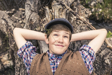 Overhead view of teen boy lying on fallen tree, hands behind head looking away smiling - ISF07007