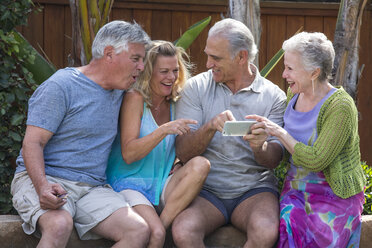 Group of seniors laughing at photos in smartphone at pool - ISF07054