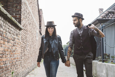 Young couple walking past brick wall - CUF18451