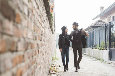 Young couple walking past brick wall - CUF18452