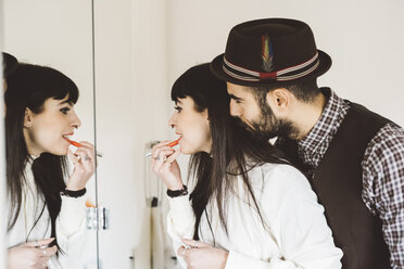 Junger Mann mit Frau beim Auftragen von Lippenstift vor einem Spiegel - CUF18462
