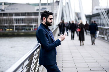 Geschäftsmann lehnt an einem Brückengeländer und liest einen Smartphone-Text, London, Großbritannien - CUF18482