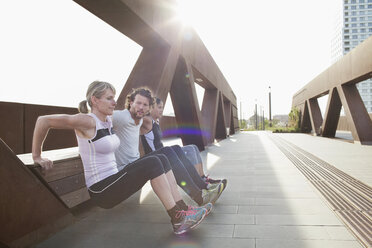 Two women and man push up training against urban footbridge - CUF18491