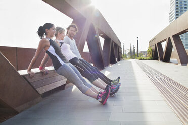 Two women and man push up training leaning against urban footbridge - CUF18492