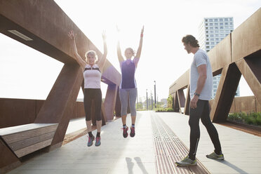 Zwei Frauen springen beim Training auf einer Fußgängerbrücke mit einem männlichen Personal Trainer - CUF18494