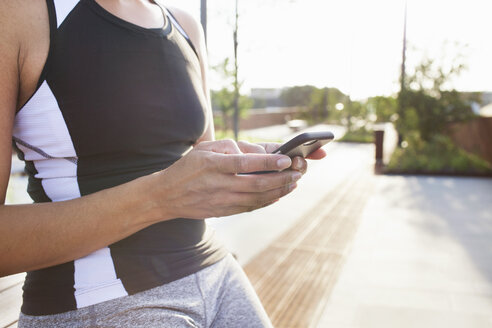 Ausgeschnittene Aufnahme einer Frau beim Training auf einer Fußgängerbrücke, die Smartphone-Texte liest - CUF18503