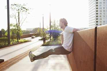 Man training raising his legs on urban footbridge - CUF18504