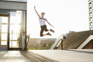 Woman training, jumping mid air on footbridge - CUF18511