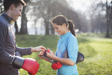 Junger Mann und Frau ziehen Boxhandschuhe zum Training im Park an - CUF18530