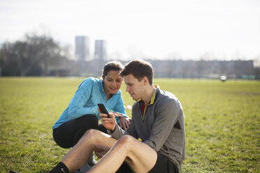 Young man and woman training, reading smartphone texts in park - CUF18536