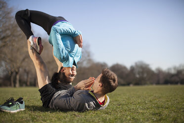 Junge Frau balanciert auf einem Mann, der im Park eine Yoga-Pose einnimmt - CUF18537