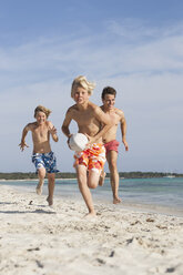 Boy running with rugby ball chased by brother and father on beach, Majorca, Spain - CUF18542