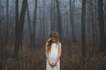 Porträt eines langhaarigen blonden Mädchens mit gesenktem Kopf im nebligen Wald - ISF07067