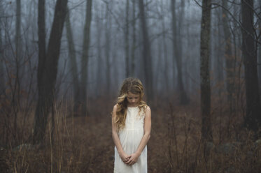 Portrait of long blond haired girl with head bowed in misty forest - ISF07067