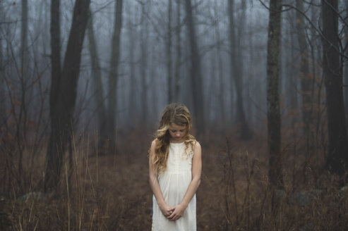 Porträt eines langhaarigen blonden Mädchens mit gesenktem Kopf im nebligen Wald - ISF07067