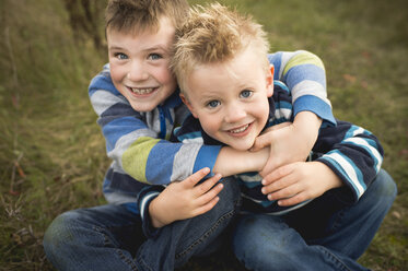Cropped view of boys sitting on grass hugging, looking at camera smiling - ISF07070