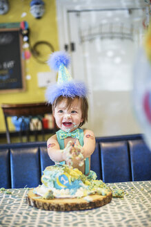 Kleiner Junge mit Partyhut zerschlägt erste Geburtstagstorte am Tisch - ISF07088