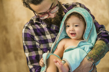 Junger Mann trägt seinen kleinen Sohn in ein Handtuch gewickelt - ISF07090