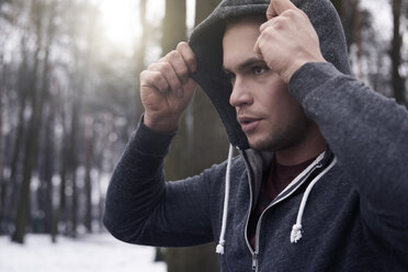 Young man wearing hooded sweatshirt, in snowy, rural landscape - CUF18681