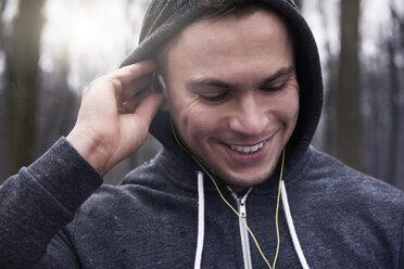 Young man outdoors, wearing hooded sweatshirt and earphones, smiling - CUF18682